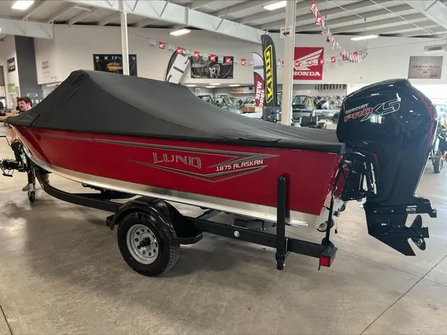 Slide: The Image of 2024 Lund 1875 Alaskan DC boat with cover in showroom, featuring Mercury outboard motor. - 6