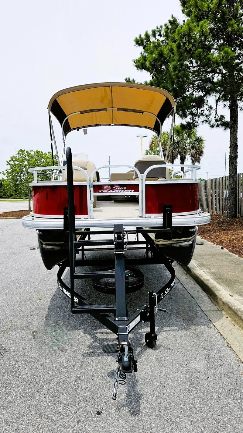Slide: The Image of 2025 Sun Tracker Bass Buggy 18 DLX pontoon boat on trailer, parked near trees. - 5