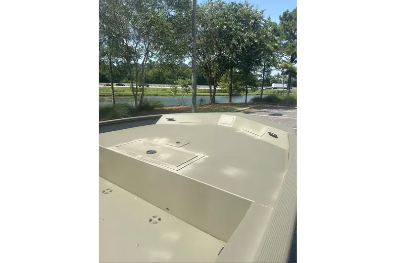 Slide: The Image of 2025 Tracker Grizzly 1860 Utility boat, spacious deck, parked near trees and water. - 6