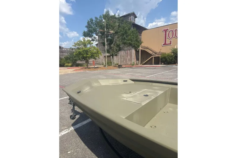 Slide: The Image of 2025 Tracker Grizzly 1860 Utility boat in a parking lot, rustic building background. - 2