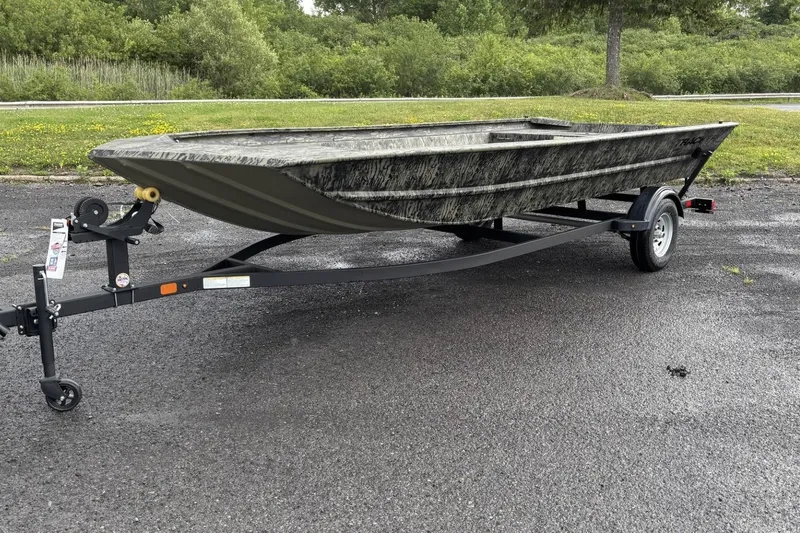 Slide: The Image of 2025 Tracker Grizzly 1860 Utility boat on trailer, parked on asphalt with greenery background. - 2
