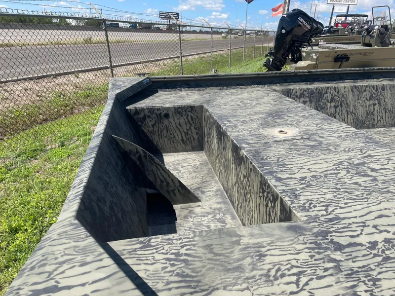 Slide: The Image of 2025 Tracker GRIZZLY 1860 Utility boat with camouflage interior, parked near a fence. - 7