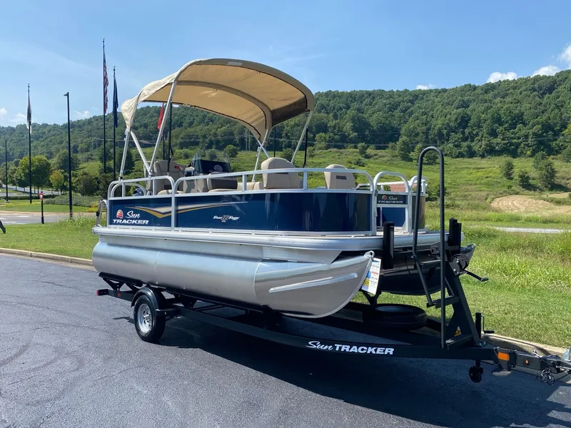 Slide: The Image of 2025 Sun Tracker Bass Buggy 16 XL Select pontoon boat on trailer, parked outdoors. - 3