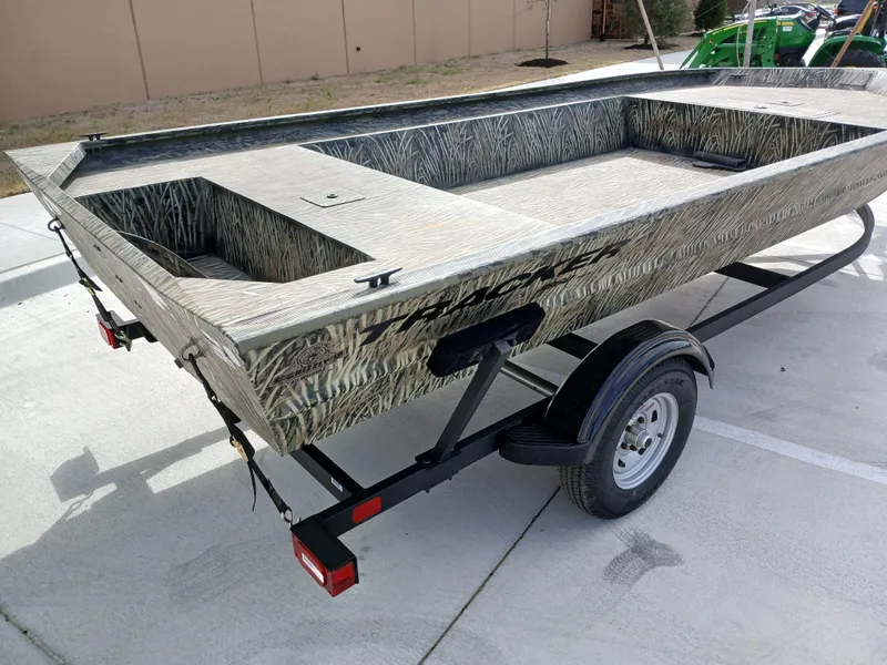 Slide: The Image of 2025 Tracker GRIZZLY 1860 Utility boat on trailer, camouflage design, parked outdoors. - 5