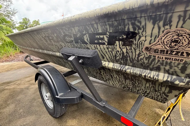 The Image of 2025 Tracker Grizzly 1860 Utility boat on trailer, featuring camo design and "All Welded" logo. - 0
