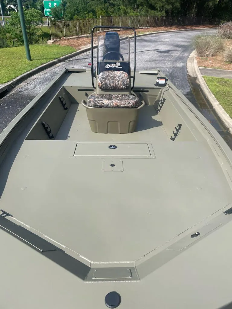 Slide: The Image of 2025 Tracker Grizzly 1860 CC boat with camouflage seating, parked on a paved path. - 2