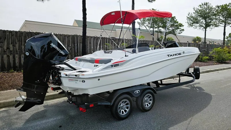 Slide: The Image of 2025 Tahoe T21 boat with red canopy on trailer, parked on street. - 2