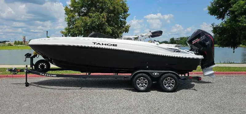 The Image of 2025 Tahoe T21 boat on trailer, parked near a lake under a blue sky. - 0