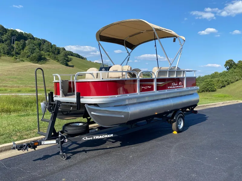 Slide: The Image of 2025 Sun Tracker Bass Buggy 18 DLX pontoon boat on trailer, parked outdoors. - 2