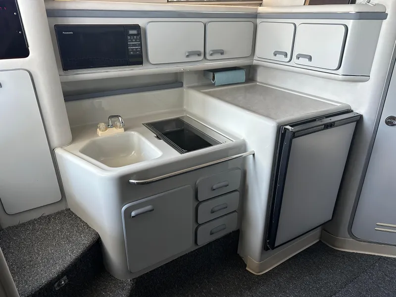 Slide: The Image of 1990 Sea Ray 310 Sundancer kitchen with sink, stove, microwave, and fridge. - 31