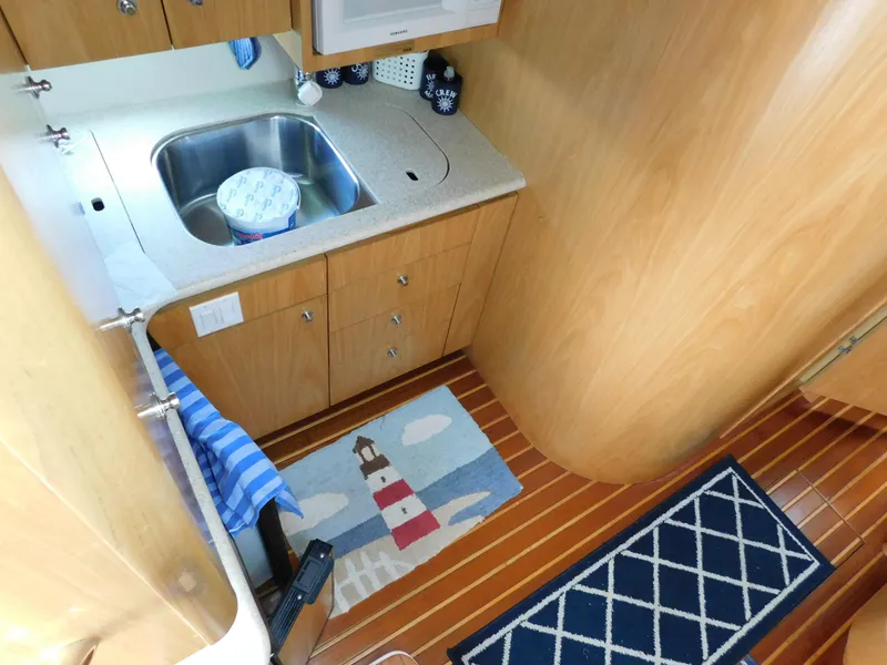 Slide: The Image of 2001 Tiara Yachts 3800 Open galley with sink, wooden cabinets, and nautical-themed rugs. - 35
