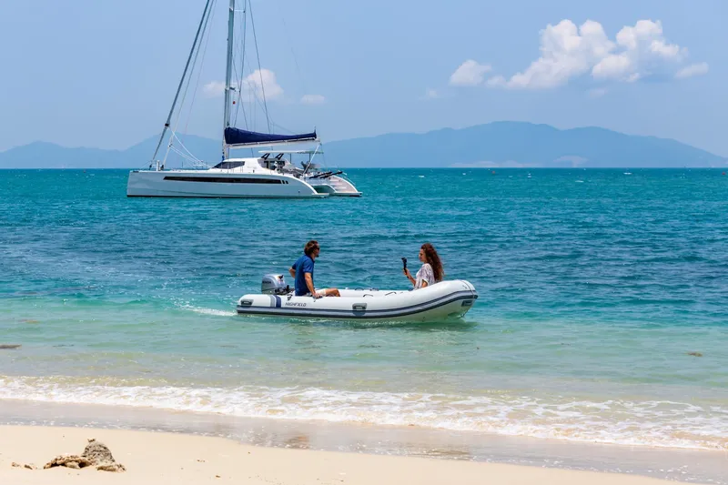 Slide: The Image of Couple in dinghy near Seawind 1600 Passagemaker catamaran, 2025, anchored by tropical beach. - 25