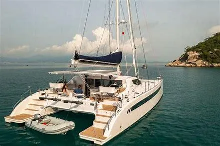 Slide: The Image of 2025 Seawind 1600 Passagemaker catamaran sailing in tranquil waters near a rocky coastline. - 26