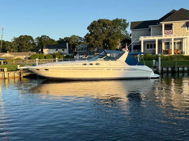 The Image of 1995 Sea Ray 400 Express Cruiser docked by waterfront homes, under clear blue sky. - 0