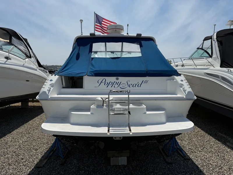 Slide: The Image of 1995 Sea Ray 400 Express Cruiser with blue cover and American flag, docked on gravel. - 10