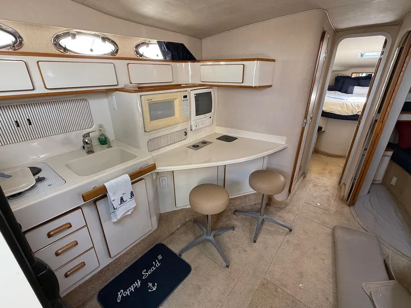 Slide: The Image of 1995 Sea Ray 400 Express Cruiser interior with kitchenette, stools, and cozy sleeping area. - 23