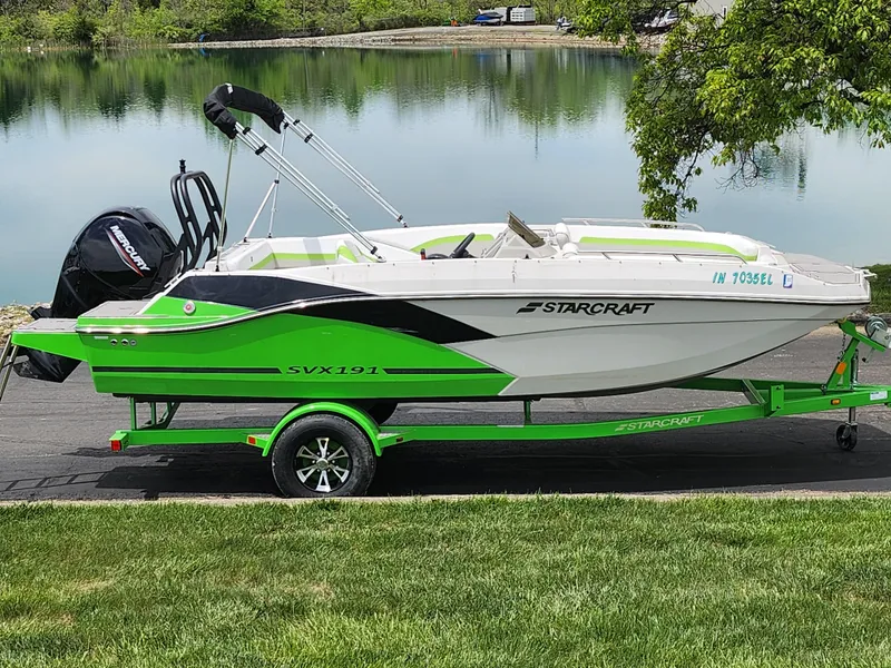 Slide: The Image of 2023 Starcraft SVX 191 OB boat on a vibrant green trailer by a lake. - 0