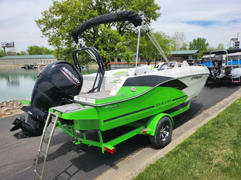 Slide: The Image of 2023 Starcraft SVX 191 OB boat in vibrant green, parked on a trailer by a lakeside. - 1