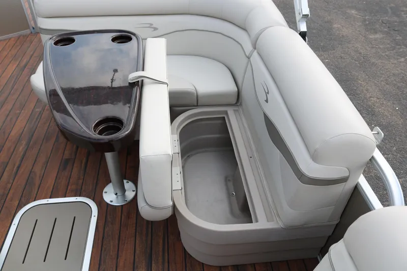 Slide: The Image of 2015 Bennington 22SSLDX boat interior with seating, storage, and table on wooden deck. - 24