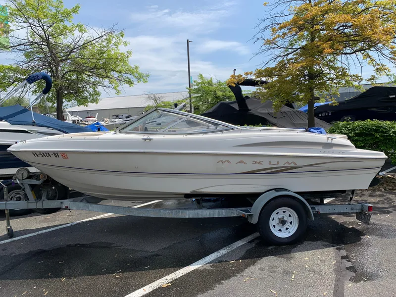 Slide: The Image of 2001 Maxum 1800 SR boat on trailer in parking lot, surrounded by trees. - 1