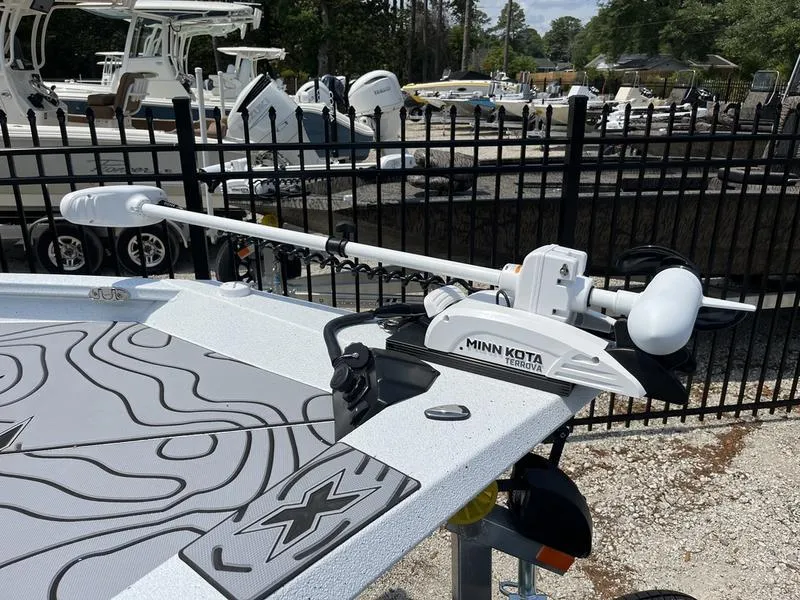 Slide: The Image of 2025 Xpress H22B boat with Minn Kota trolling motor, docked near black fence. - 19