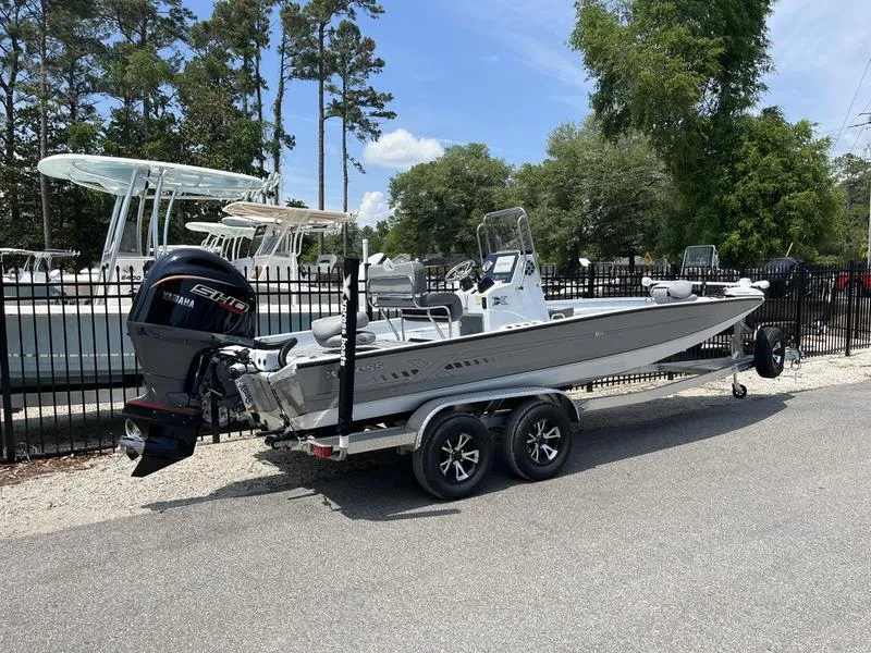 Slide: The Image of 2025 Xpress H22B boat on trailer, parked outdoors near trees and other boats. - 2