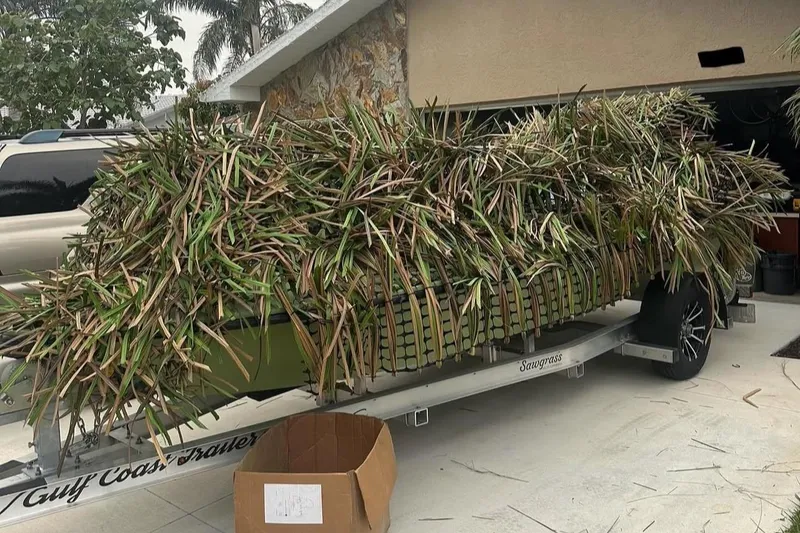 Slide: The Image of 2025 Sawgrass 17 boat camouflaged with foliage on a trailer in a driveway. - 11