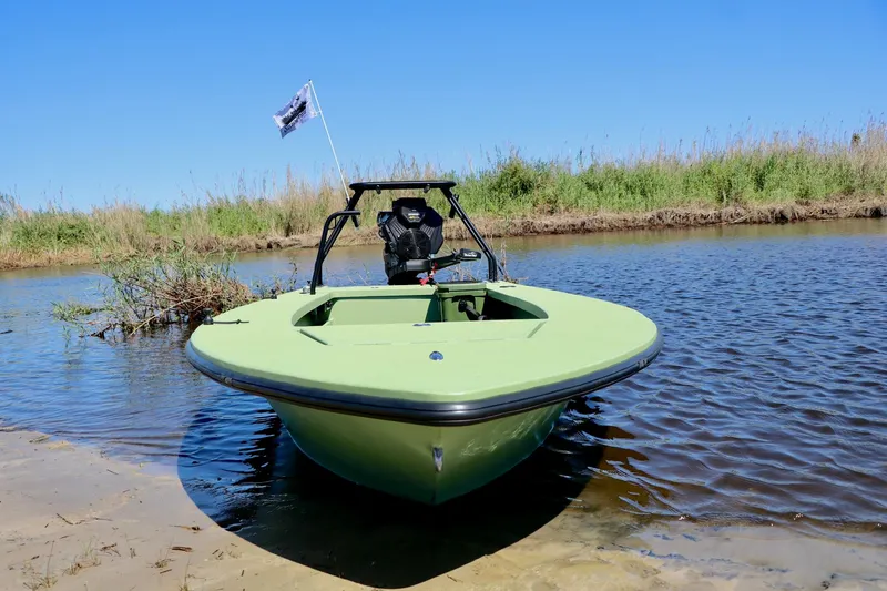 Slide: The Image of 2025 Sawgrass 17 boat in shallow water, green hull, clear sky, grassy shoreline. - 4