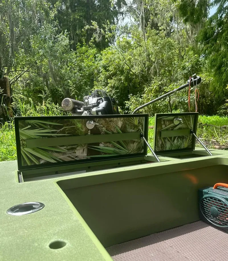 Slide: The Image of Sawgrass 17 boat, 2025 model, with open storage compartments in a lush, green forest setting. - 7