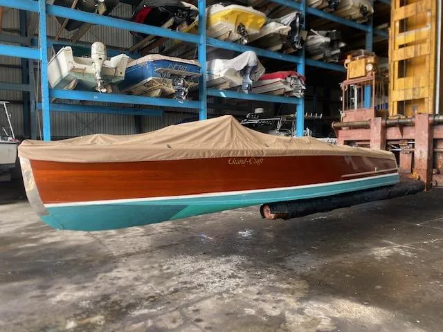 Slide: The Image of Grand Craft Classic Runabout 2000 in storage, covered, with wooden hull and teal bottom. - 13