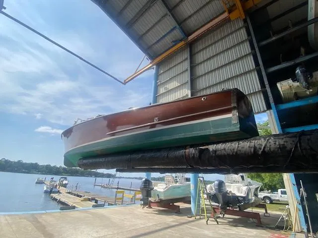 Slide: The Image of Grand Craft Classic Runabout 2000 in a boatyard, suspended for maintenance by the water. - 5