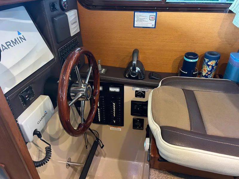 Slide: The Image of 2016 Ranger Tugs R-25SC helm with Garmin navigation, wooden steering wheel, and comfortable seating. - 28