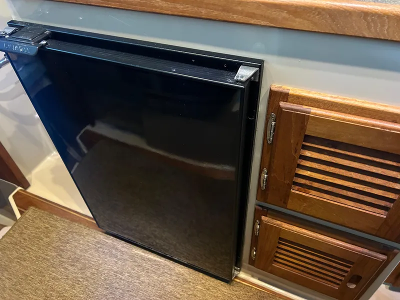 Slide: The Image of 2016 Ranger Tugs R-25SC interior with black fridge and wooden cabinets. - 36