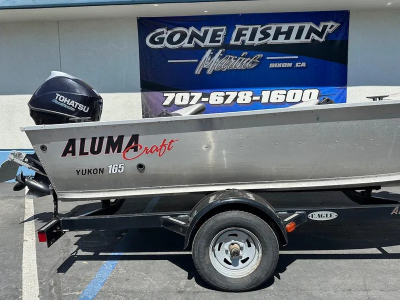 Slide: The Image of 2018 Alumacraft Yukon 165 boat on trailer, Tohatsu motor, "Gone Fishin'" banner in background. - 6
