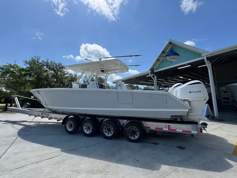 Slide: The Image of 2018 Jupiter 34 HFS boat on trailer, parked outside a building under a clear sky. - 18