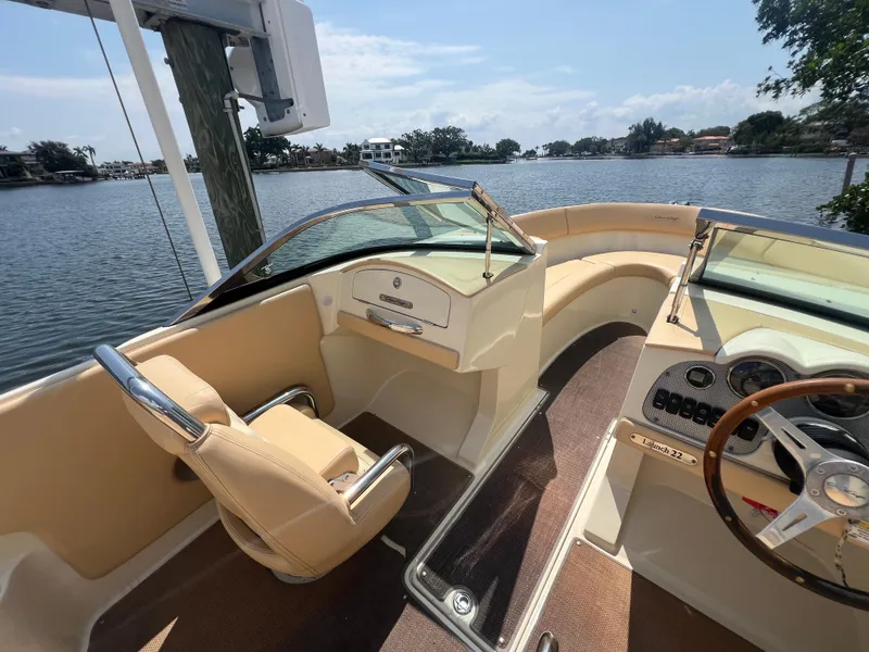 Slide: The Image of 2013 Chris-Craft Launch 22 boat interior with beige seating and steering wheel, docked by a lake. - 4