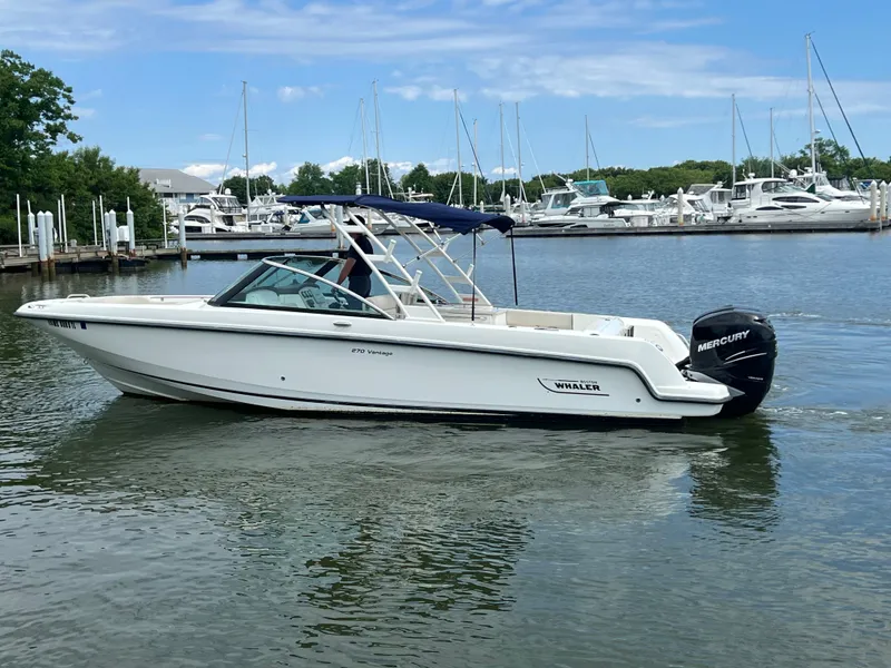Slide: The Image of 2016 Boston Whaler 270 Vantage boat on calm marina waters, surrounded by yachts. - 16