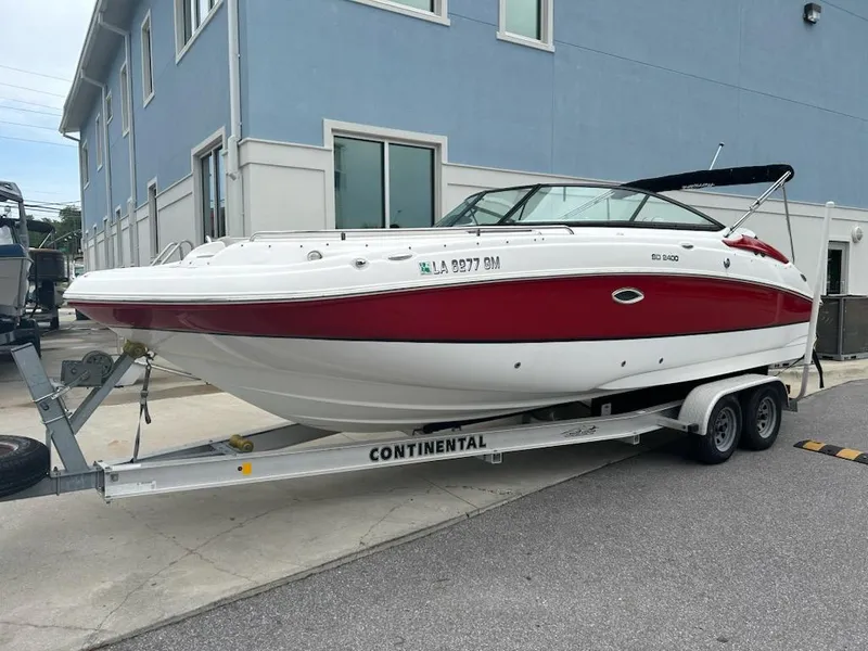Slide: The Image of 2021 Hurricane SunDeck 2400 OB boat on trailer, parked near a blue building. - 0