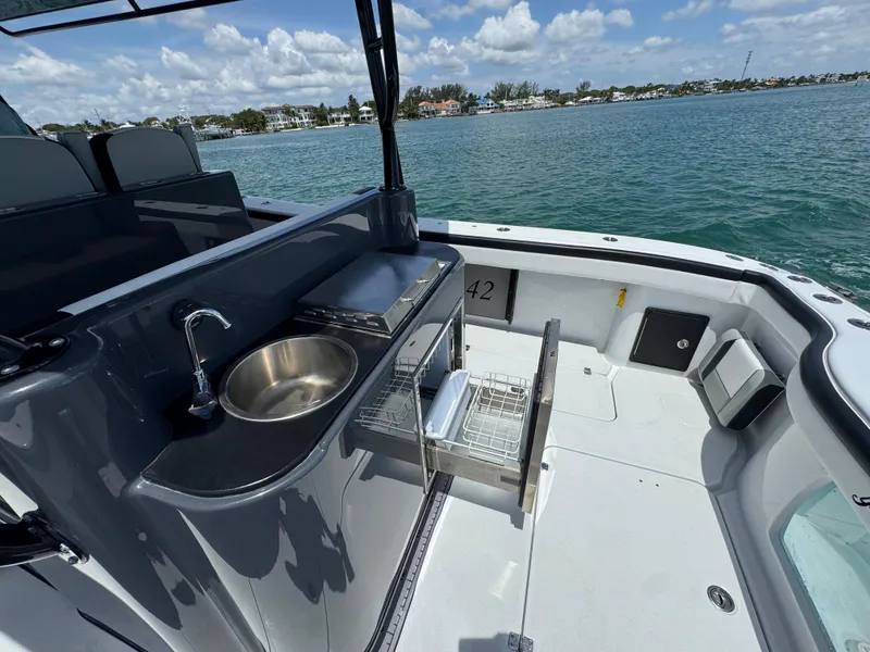 Slide: The Image of 2023 Yellowfin 42 boat deck with sink and storage, overlooking calm waters and distant shoreline. - 22