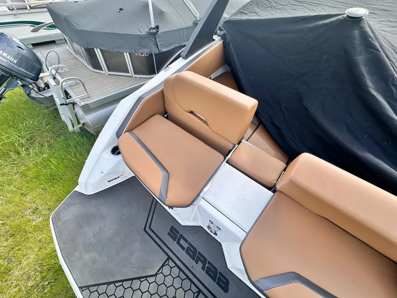 Slide: The Image of 2021 Scarab 195 Jet Boat with tan seating and black cover, docked near grass. - 3