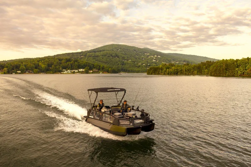 Slide: The Image of 2025 Sea-Doo Switch™ Fish 21 cruising on a scenic lake with lush hills in the background. - 12