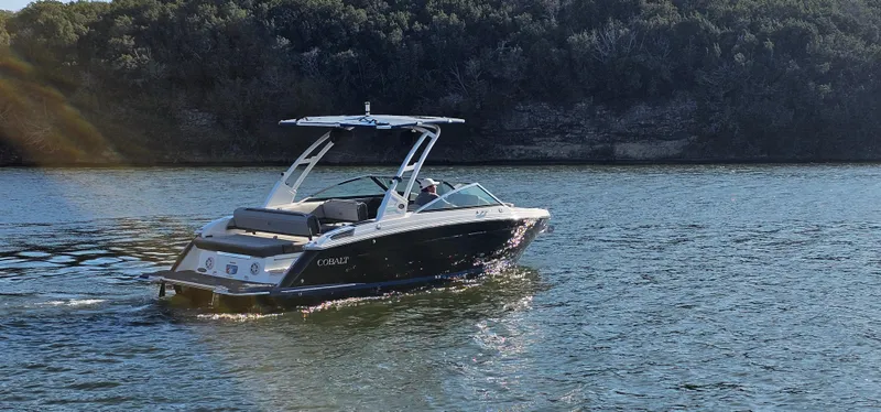 Slide: The Image of 2022 Cobalt R6 boat cruising on a calm lake with lush green shoreline. - 2