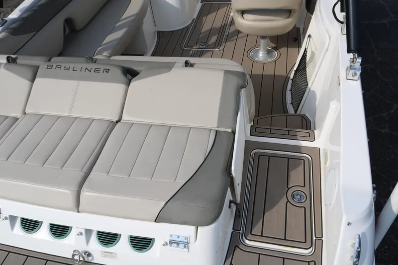 Slide: The Image of 2016 Bayliner 215 Deck Boat interior with beige seating and wood-style flooring. - 14