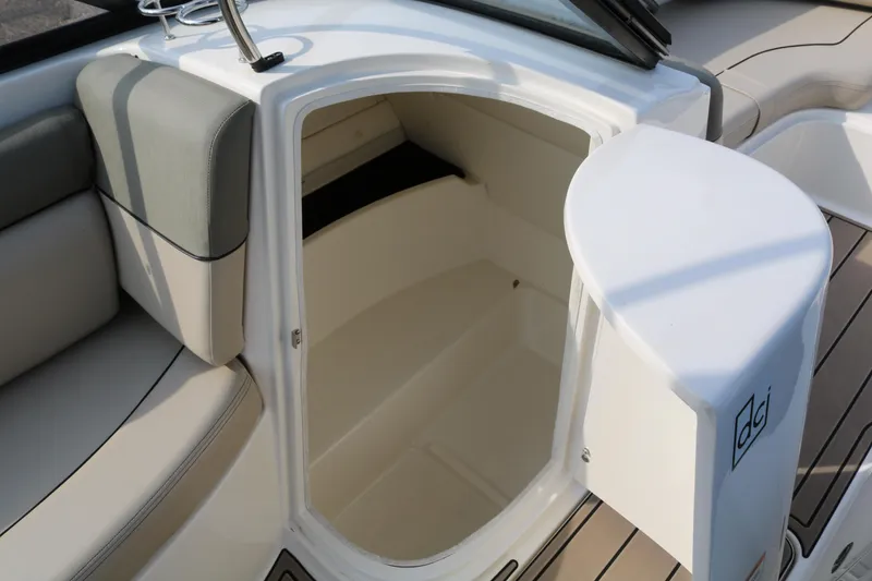 Slide: The Image of 2016 Bayliner 215 Deck Boat interior storage compartment with open door, showcasing seating and flooring. - 33