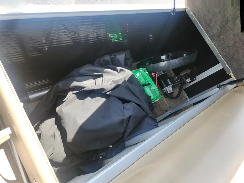 Slide: The Image of Storage compartment of a 2018 Sweetwater 2086 C, containing a black cover and green battery. - 15