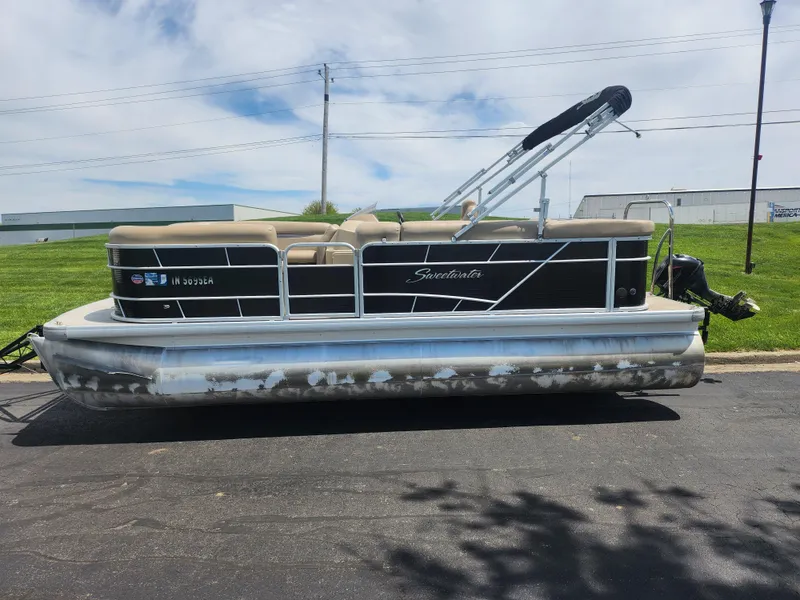 Slide: The Image of 2018 Sweetwater 2086 C pontoon boat parked on pavement, featuring beige seating and black accents. - 4
