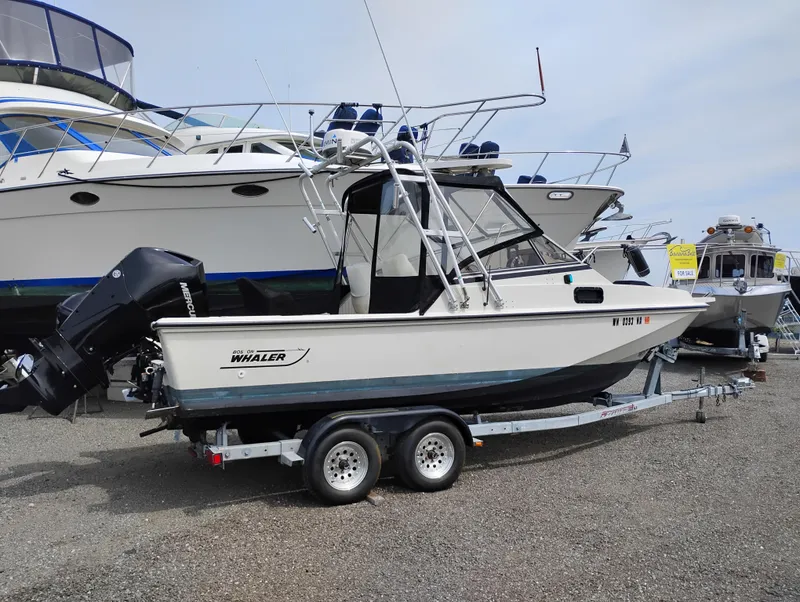The Image of 1989 Boston Whaler 22 Renegade Cabin on trailer, parked beside other boats. - 0