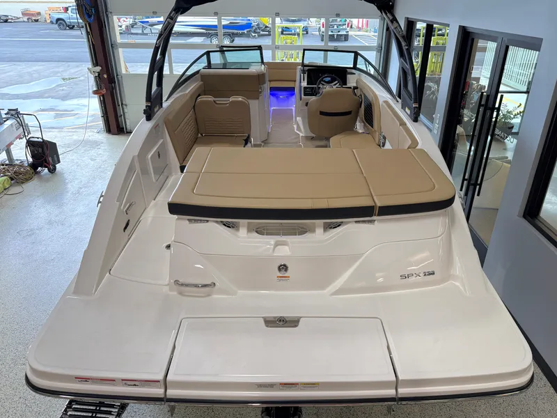 Slide: The Image of 2025 Sea Ray SPX230 boat with tan seating, viewed from the rear in a showroom. - 23