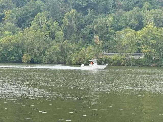 Slide: The Image of 2025 Caymas 24 HB boat cruising on a scenic, tree-lined river. - 32