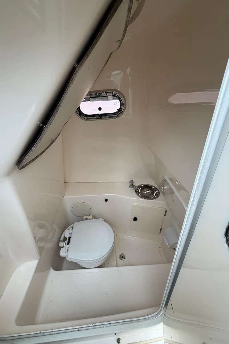 Slide: The Image of 2008 Pursuit 2570 CC boat interior with compact marine toilet and small window. - 22